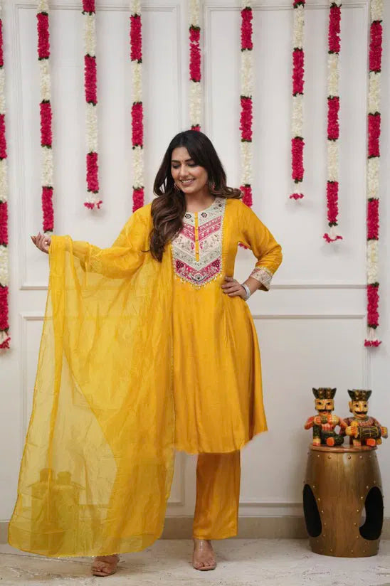 Woman in a yellow traditional outfit standing in front of floral decorations.