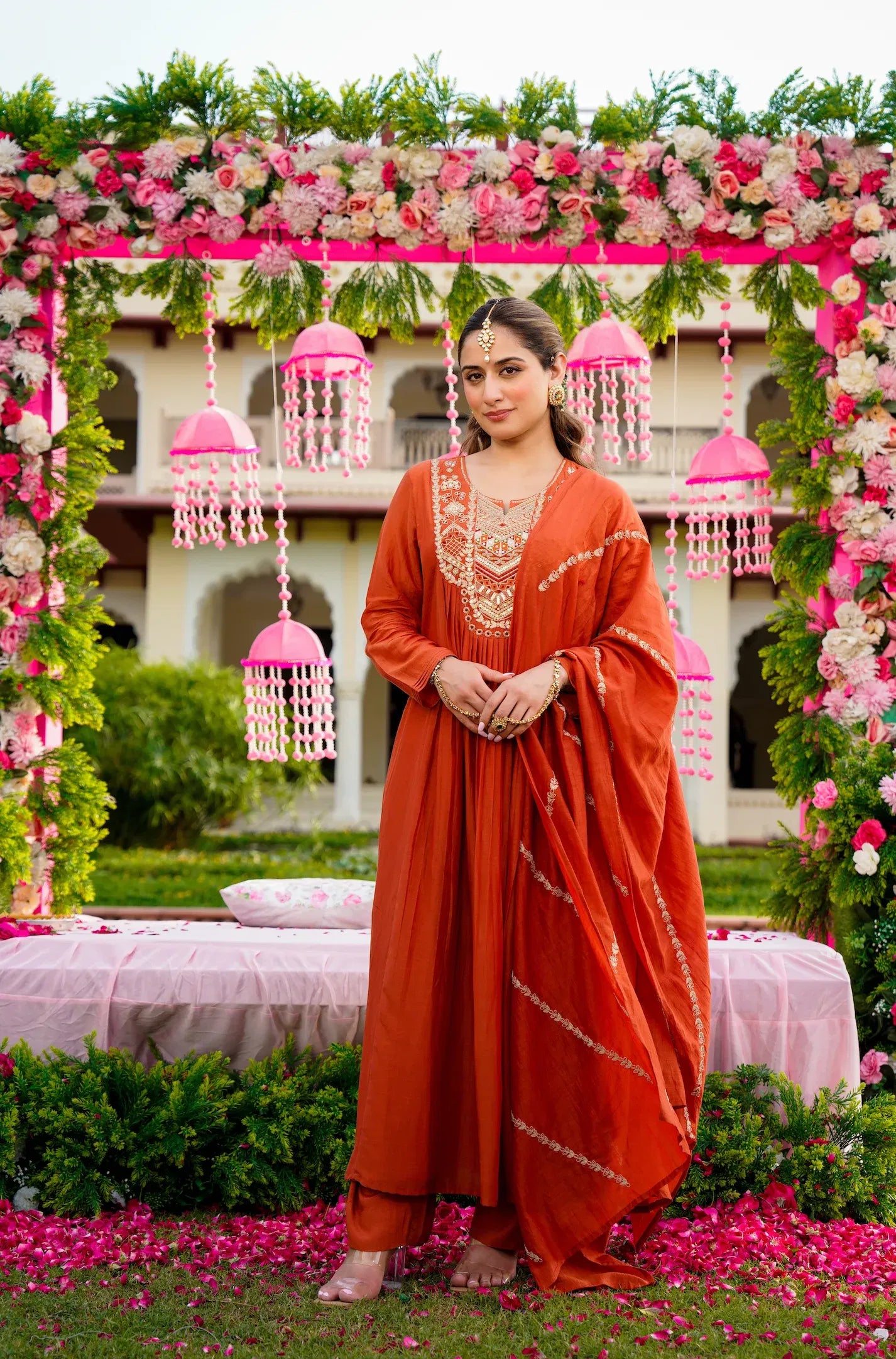 Woman in an orange traditional outfit standing in front of a decorated floral archway.