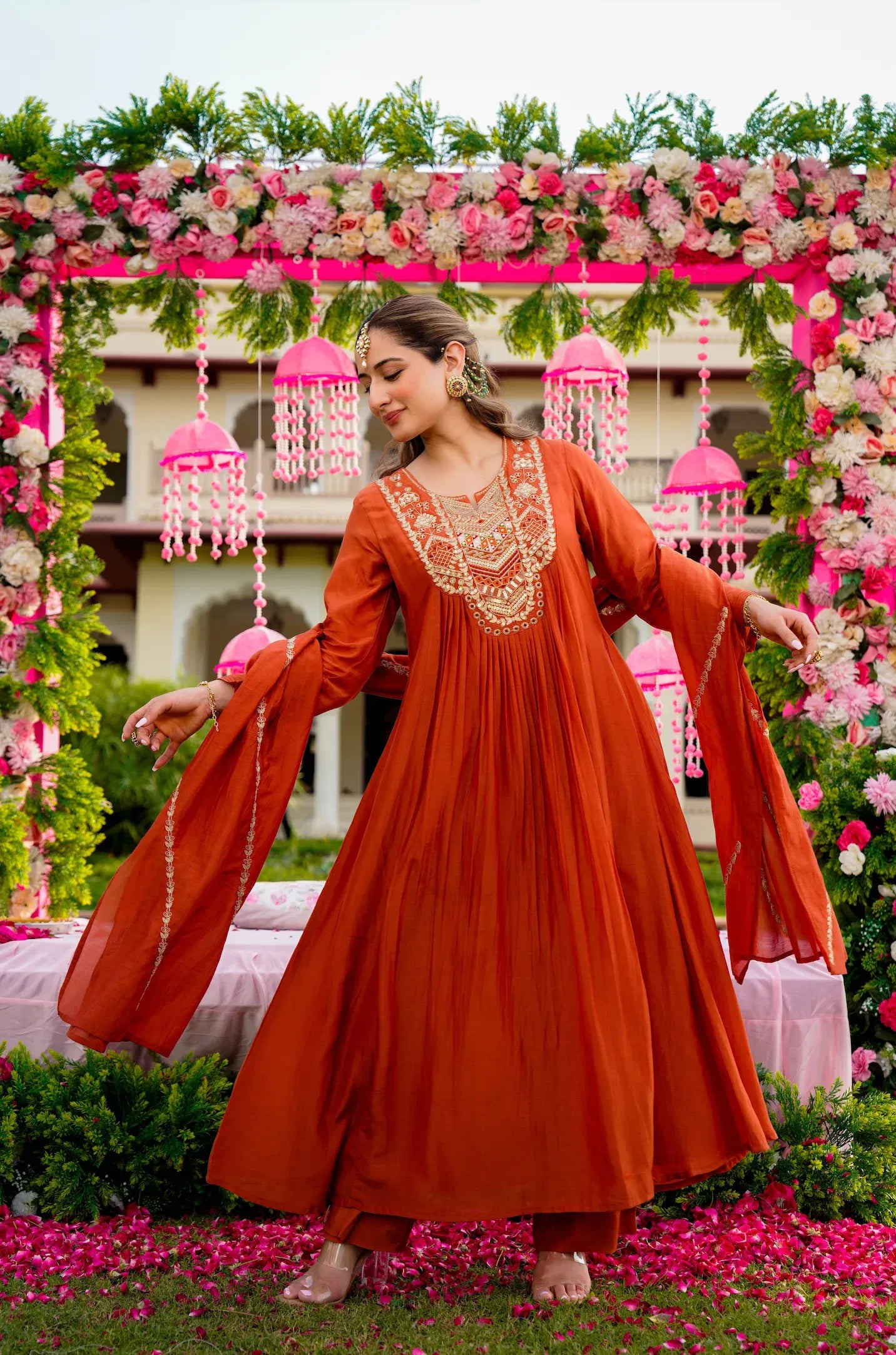 Woman in an orange traditional outfit standing in front of a decorated floral arch.